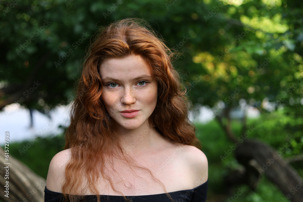 Portrait of pretty ginger girl with long red hair and freckles standing in summer park. Young sensual model, natural female beauty Portrait of pretty ginger girl with long red hair and freckles standing in summer park. Young sensual model, natural female beauty