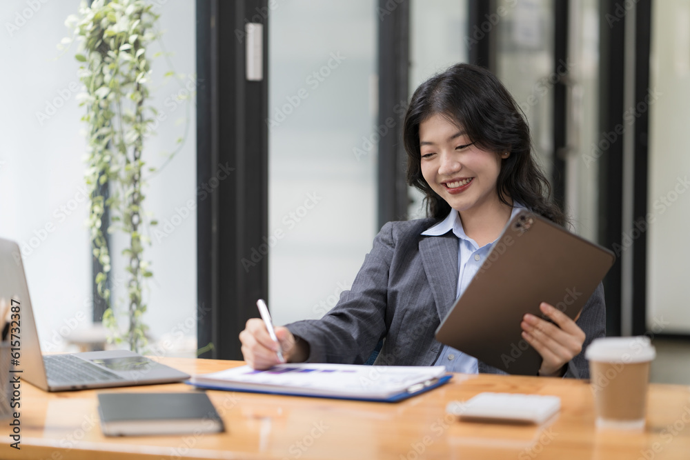 Attractive business Asian woman using a digital tablet while sitting at a workplace desk in an office. Attractive business Asian woman using a digital tablet while sitting at a workplace desk in an office.
