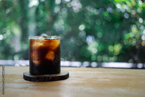 Ice coffee in a glass on a nature background. Cold summer drink with copy space