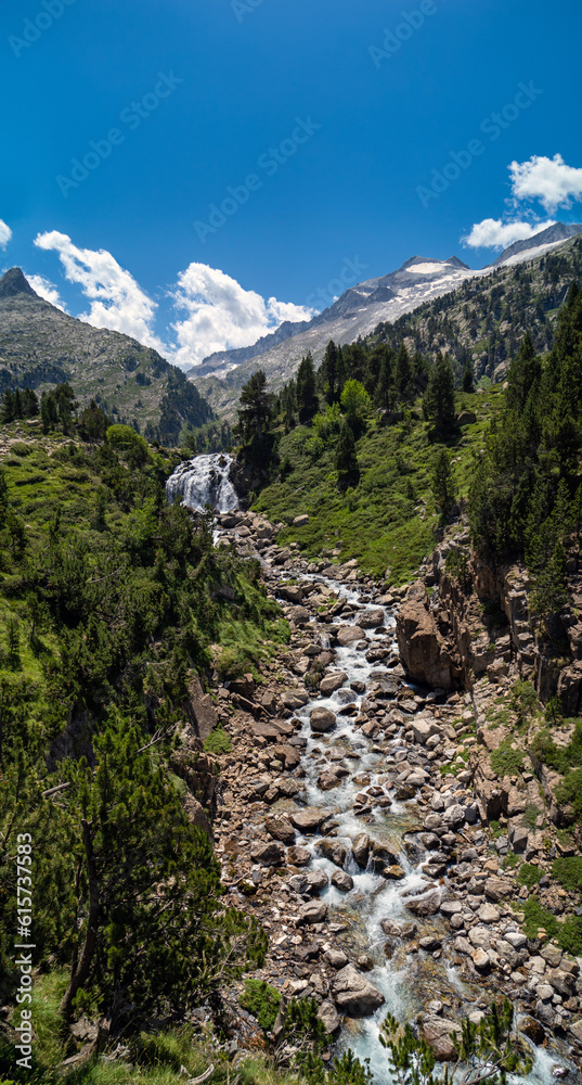 Spectacular vertical view of the river water falling from the Forau Aigualluts waterfall between the large stones in the Aragonese Pyrenees of Benasque. Blue clean sky and mountains with snow.
