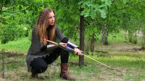 Smooth camera movement, selective focus, a young woman in chain mail and bracers with a bow in her hands sits against the backdrop of a summer forest.