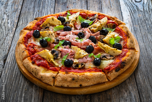 Pizza capricciosa with cooked ham, mozzarella, artichoke and vegetables on wooden table 