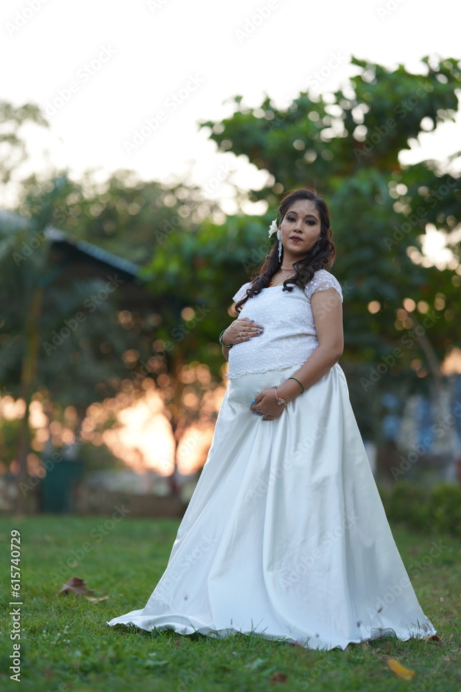 Beautiful happy Asian, Indian pregnant woman holding her belly at home and looking at the camera with a smile.