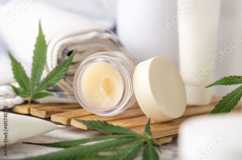 Jar with CBD lip balm near green cannabis leaves near bottles and towel close up