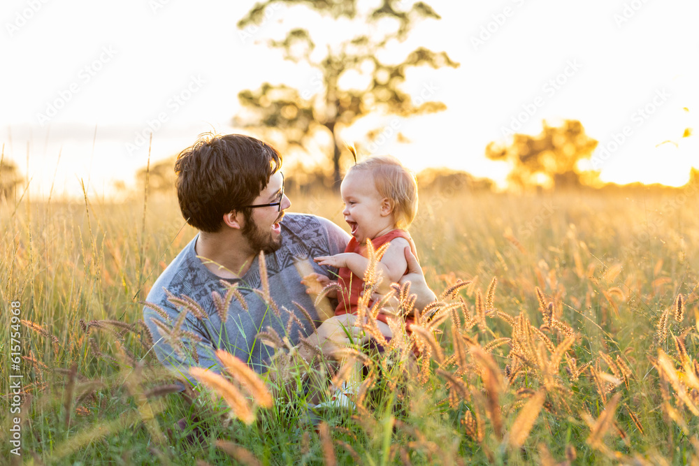 Happy family time with dad and daughter laughing together in long grass of farm paddock in country Happy family time with dad and daughter laughing together in long grass of farm paddock in country