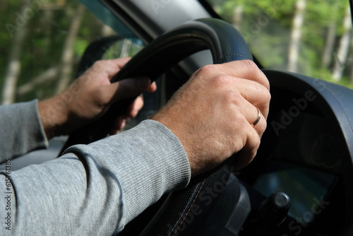Male Hands holding steering wheel close up. Confident man driving a car during jorney trip. Side view from passenger inside car interior. Summer day. Driver. Selective Focus, Cropped. Travel concept photo