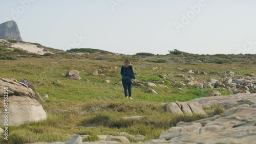 Young woman walking on grass with stones and mountain in background at cape point national park