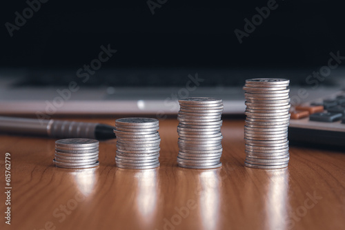 Stack of money coin on wood desk with laptop computer in the background, Business and Financial concept. 