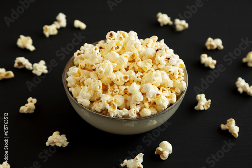 Healthy Buttered Popcorn with Salt in a Bowl on a black background, side view.