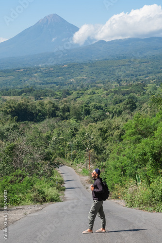 A male traveler with a backpack travels alone, walking along the road towards the volcano.