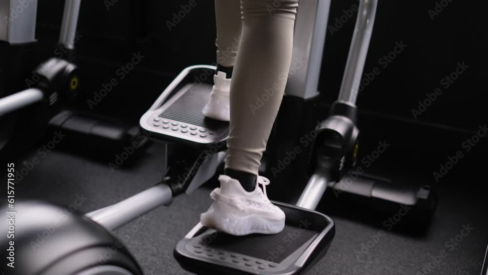Women's legs in sneakers work on a stepper in the gym. The concept of sport and healthy lifestyle. The girl is doing exercises.