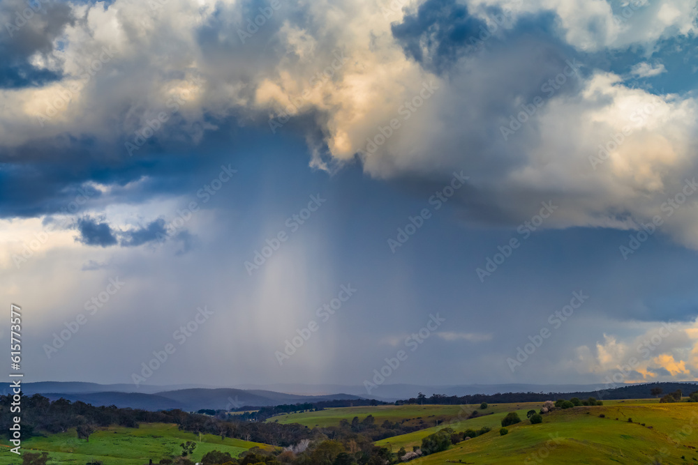 Distant view of heavy rain falling from a dramatic cloud over a green valley Distant view of heavy rain falling from a dramatic cloud over a green valley