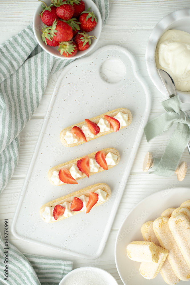 The process of making a dessert of Savoyard cookies, strawberries and buttercream. The photo is part of a group of photos where the creation of the dessert is shown step by step The process of making a dessert of Savoyard cookies, strawberries and buttercream. The photo is part of a group of photos where the creation of the dessert is shown step by step