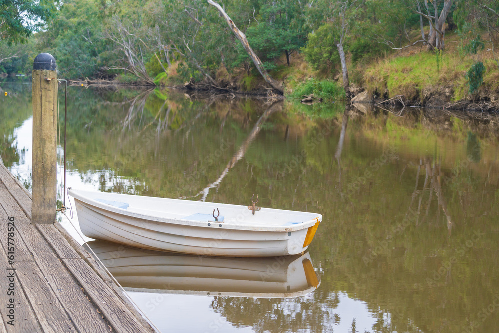 A solitary row boat tied to a bollard alongside a dock on a still river A solitary row boat tied to a bollard alongside a dock on a still river