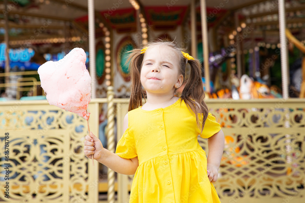 Little girl with cotton candy in an amusement park. The concept of summer holidays and school holidays