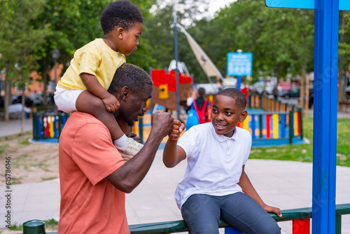 African black ethnicity father waving with his children in the playground of the city park