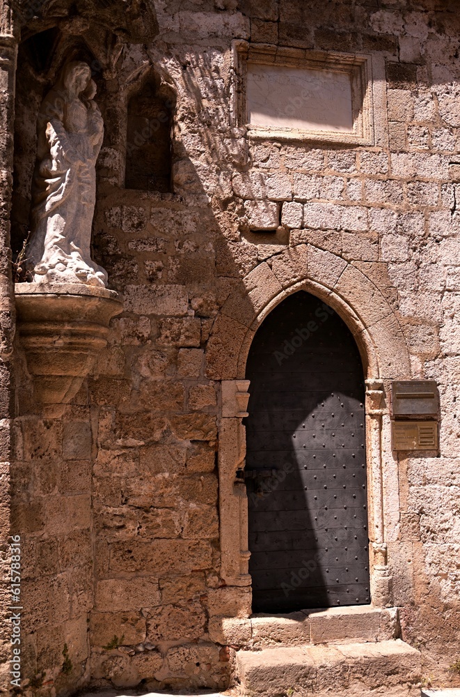 The facade of a medieval chapel with an arched door and a statue of the Virgin Mary at the entrance, located on the street of the knights in Rhodes.