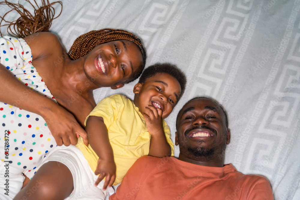 Portrait of African black ethnicity family with their little son in the bedroom on the bed smiling, overhead shot