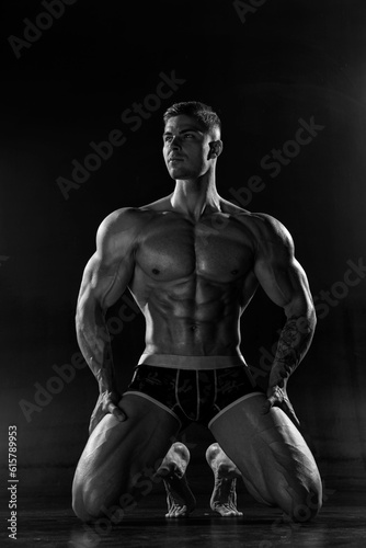 Muscular shirtless man with perfect body posing kneeling in studio
