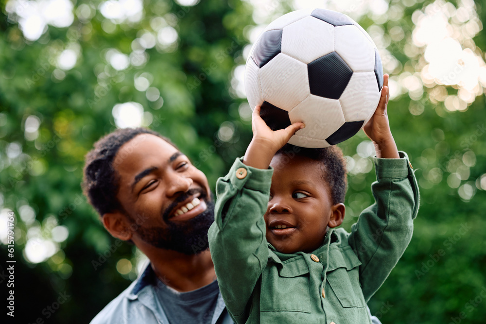 Happy black boy holds ball while playing with his father outdoors.