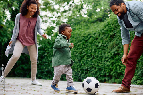 Happy black boy and his parents play with ball in backyard.