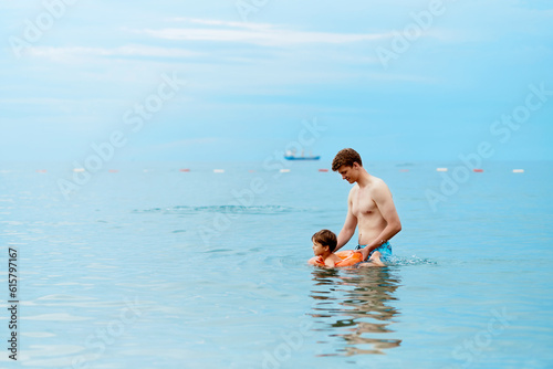 A father teaches a child to swim in the sea on an inflatable ring.