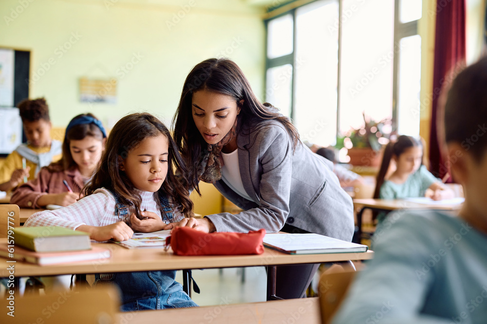 Hispanic elementary school teacher helps her student in learning in classroom.