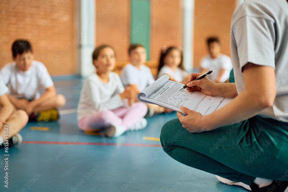 Fototapeta premium Close up of physical education teacher taking notes during exercise class at school gymnasium.