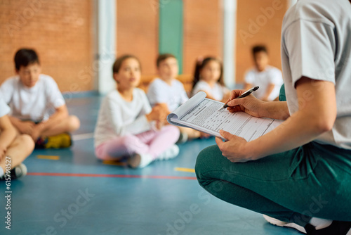 Close up of physical education teacher taking notes during exercise class at school gymnasium. © Drazen