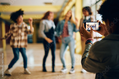 Close up of teenager using cell phone while photographing his friends at high school hallway.