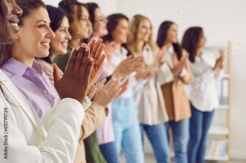 Close up photo of a group of women standing in a row in office and applouding on a meeting or seminar. Female multinational company employees clapping hands at the conference. Selective focus.