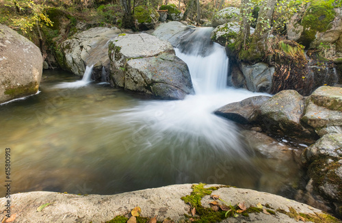 Small waterfall in a river whose flow runs between large granite stones deep in a dark forest. Concept of peace and relaxation, water stream and silk water.