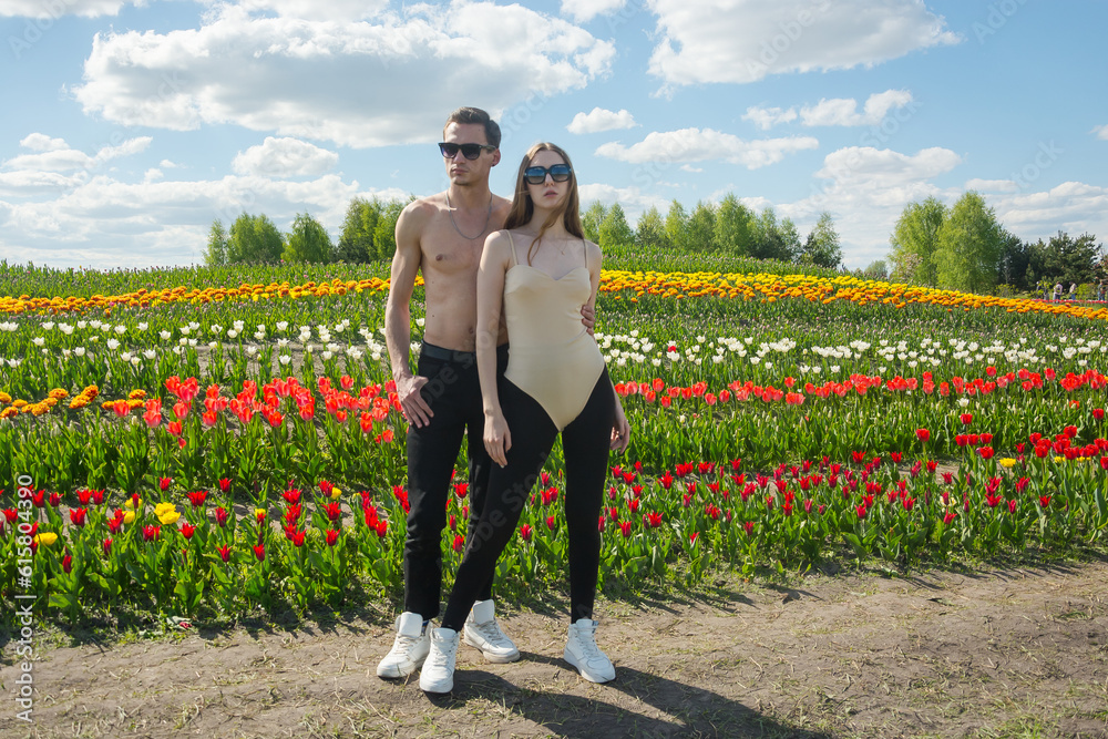 A beautiful young couple stands in sportswear at the background of a field of colorful tulips.