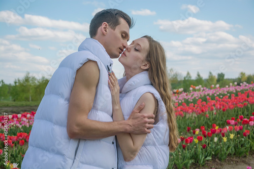 Obraz na płótnie Guy and girl are kissing and hugs at field of colorful tulips. w salonie