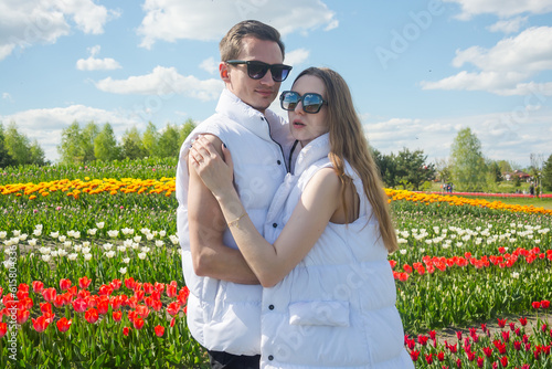 oung beautiful couple in white clothes, on the background of a field of colorful tulips.