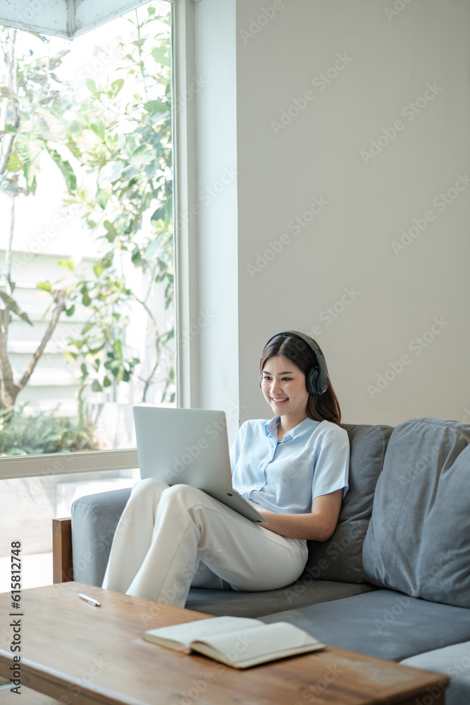 Beautiful Young asian woman at home sitting on the sofa using laptop and headphone listening to music at home. Beautiful Young asian woman at home sitting on the sofa using laptop and headphone listening to music at home.