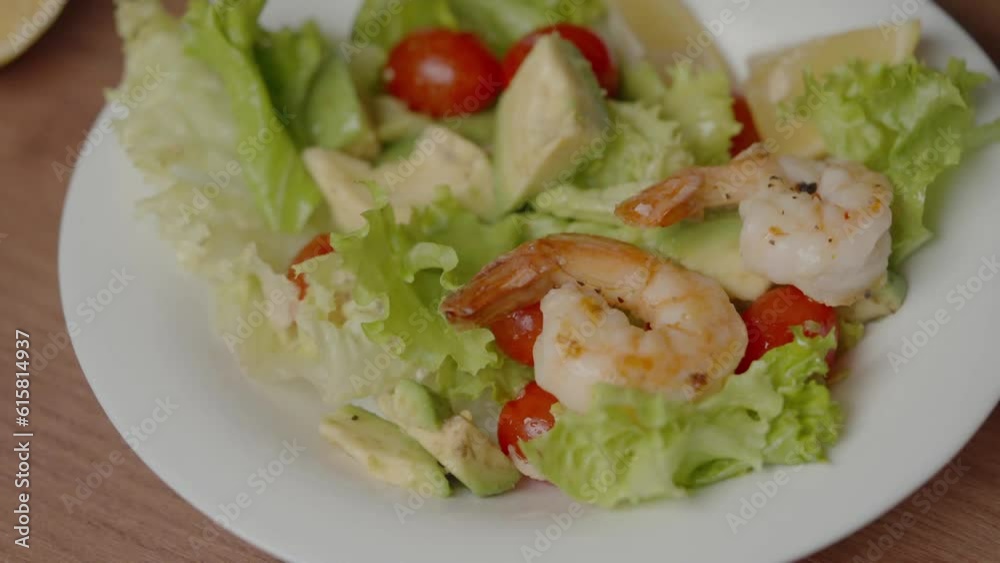 Close up top side view, glass bowl with lettuce, cherry tomatoes and avocado. Fried juicy shrimps are laid out.