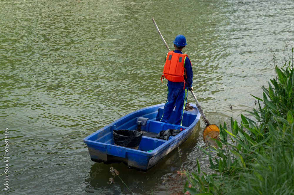 A worker stand in boat to collect garbage in river