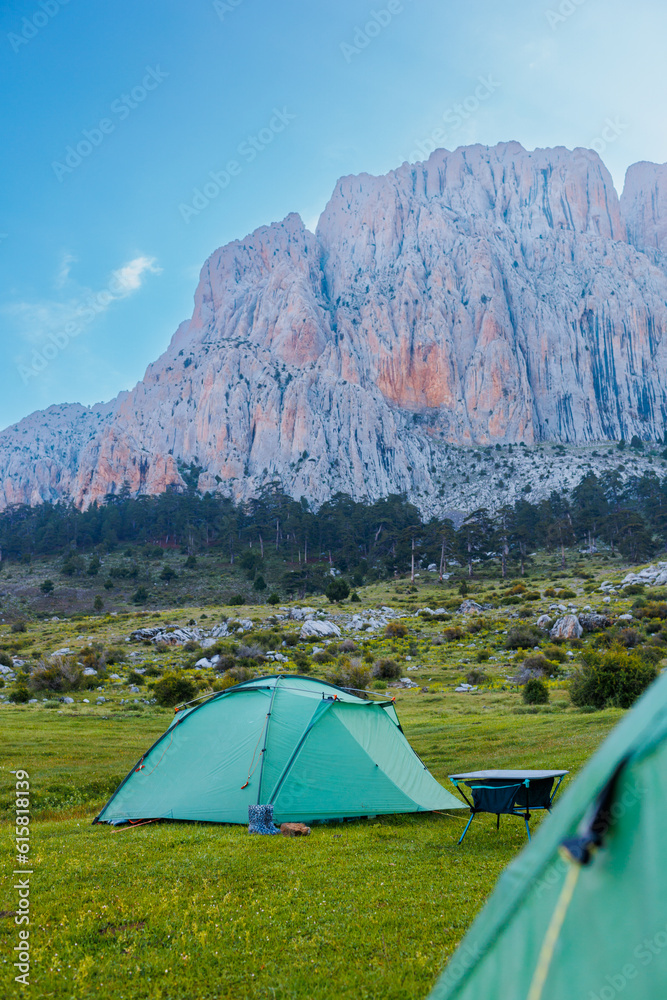 Green camping tents stand on a green meadow with beautiful mountains in the background. Spending time outdoors.