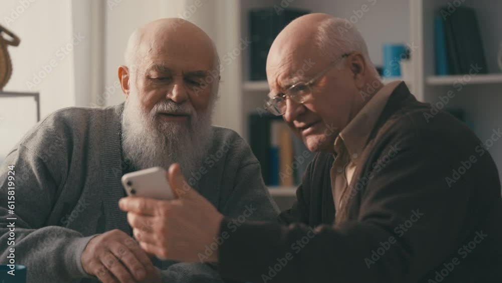 Two elderly male friends trying to install new app on phone, modern technology