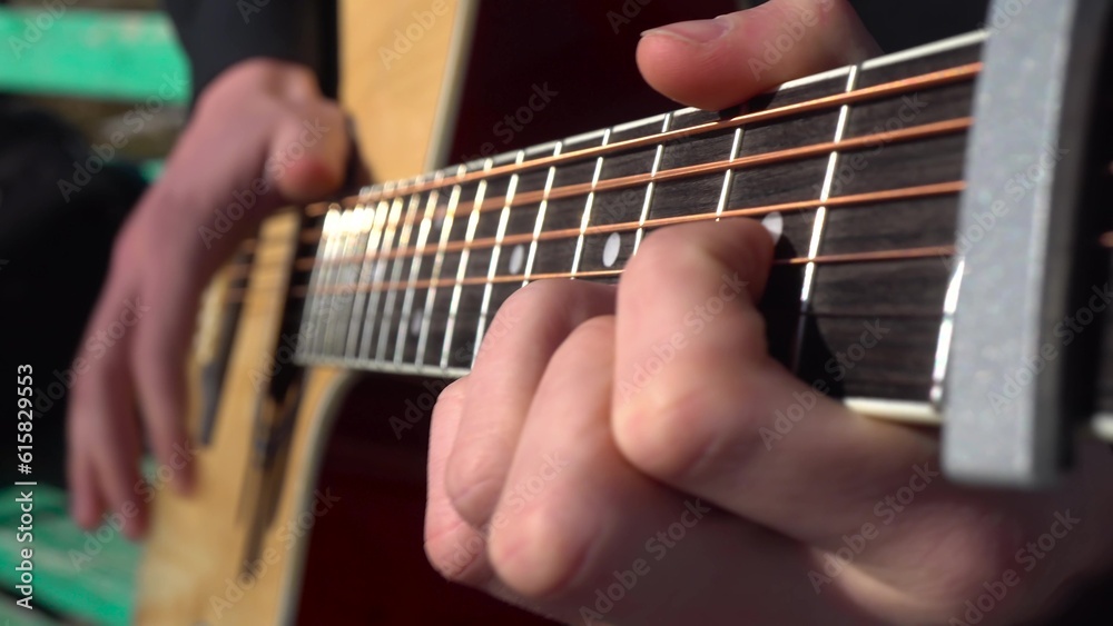 A young man plays the guitar in the park. The hand of a man closeup.