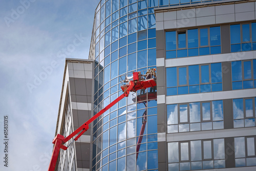 Glass facade cleaning work, workers washing windows at height of high rise building in lifting platform. Man on crane bucket washing glass facade. Window cleaner, building wet wash.
