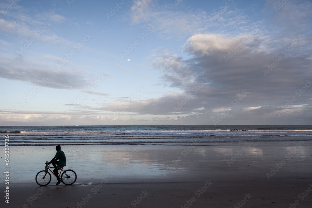Fototapeta premium Man riding a bike in the beach with ocean background - Moreré, Bahia, Brazil