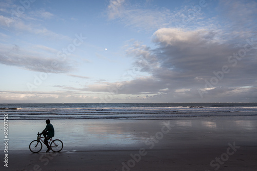 Man riding a bike in the beach with ocean background - Moreré, Bahia, Brazil