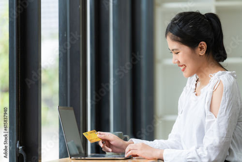 A young Asian businesswoman holding a credit card for shopping online with a computer laptop.