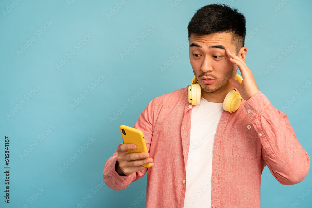 Fototapeta premium Worried man uses mobile phone and rubs his forehead.