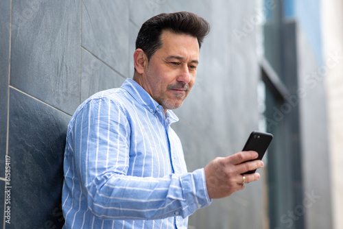 Older man leaning against wall looking at mobile phone