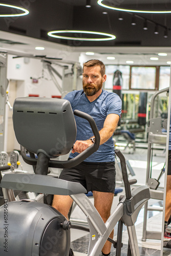 An active man with beard training in gym, riding a stationary exercise bike. Sport and quarantine.