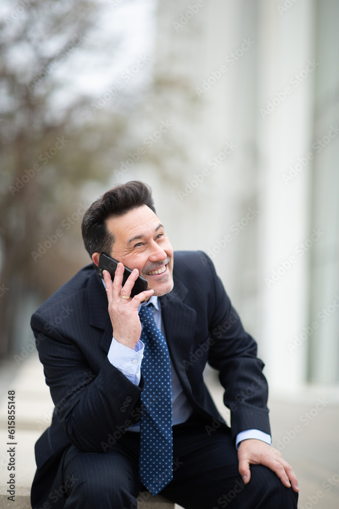 Happy mature businessman sitting outside talking on cellphone Happy mature businessman sitting outside talking on cellphone