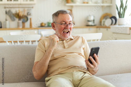 Middle aged senior man euphoric winner with smartphone. Older mature grandfather looking at cell phone reading great news getting good result winning online bid feeling amazed. Winning gesture